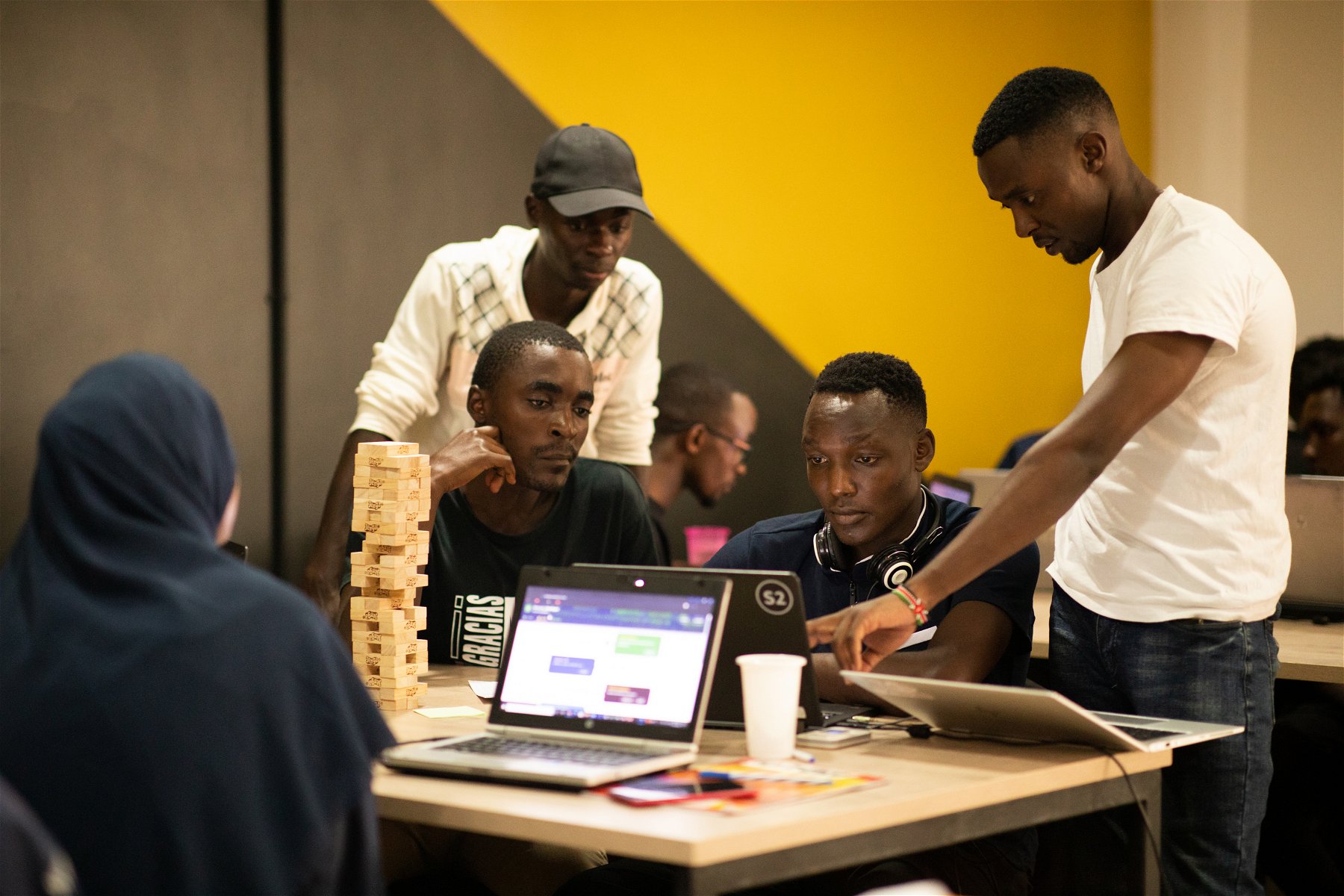 A group of young men and a woman is working on laptops.