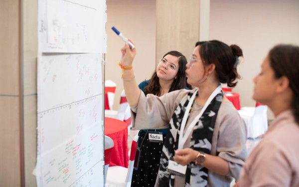 Three women are standing in front of a whiteboard at a Norec training